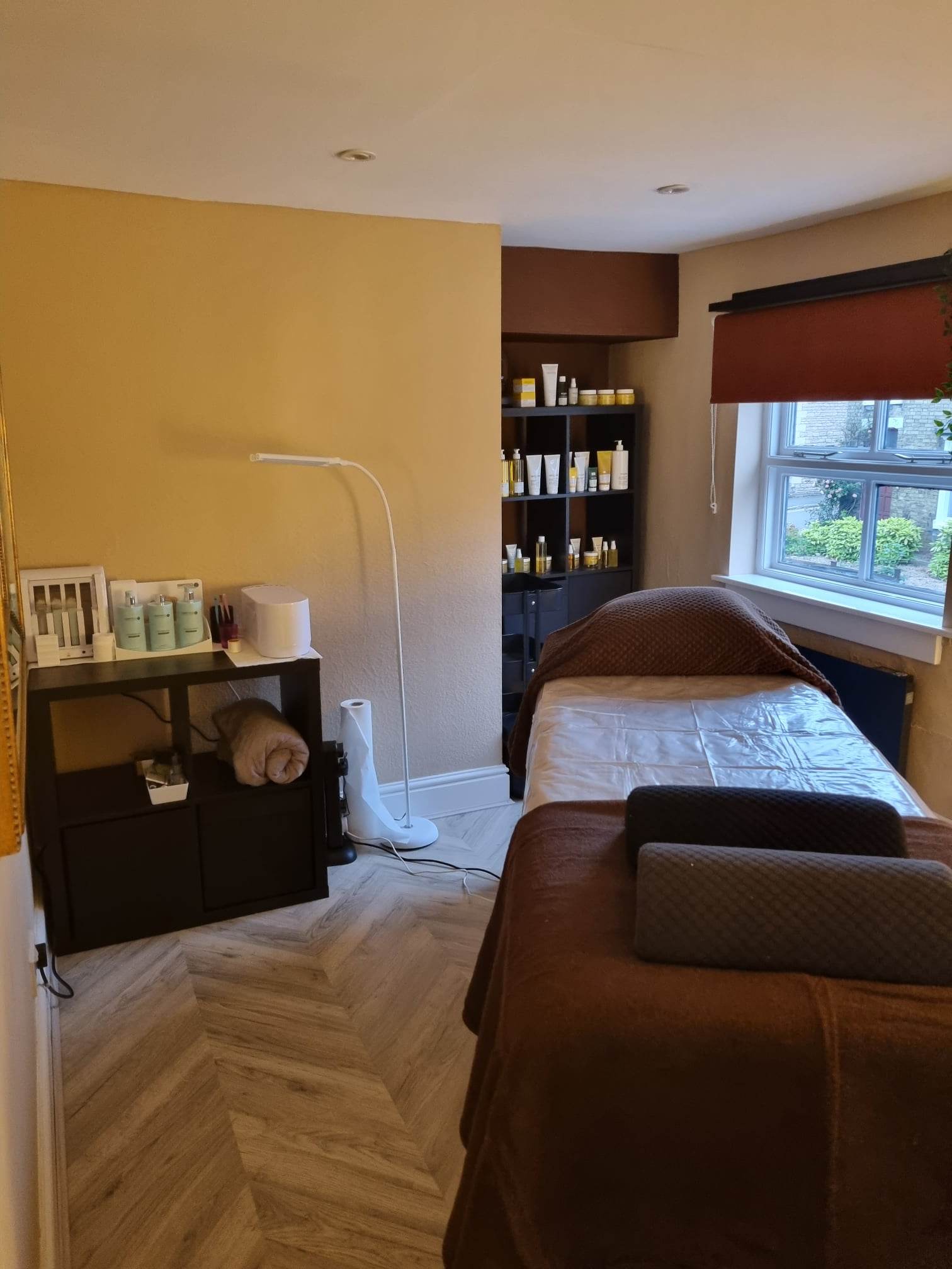 Treatment room with a made-up couch, product shelves and a window