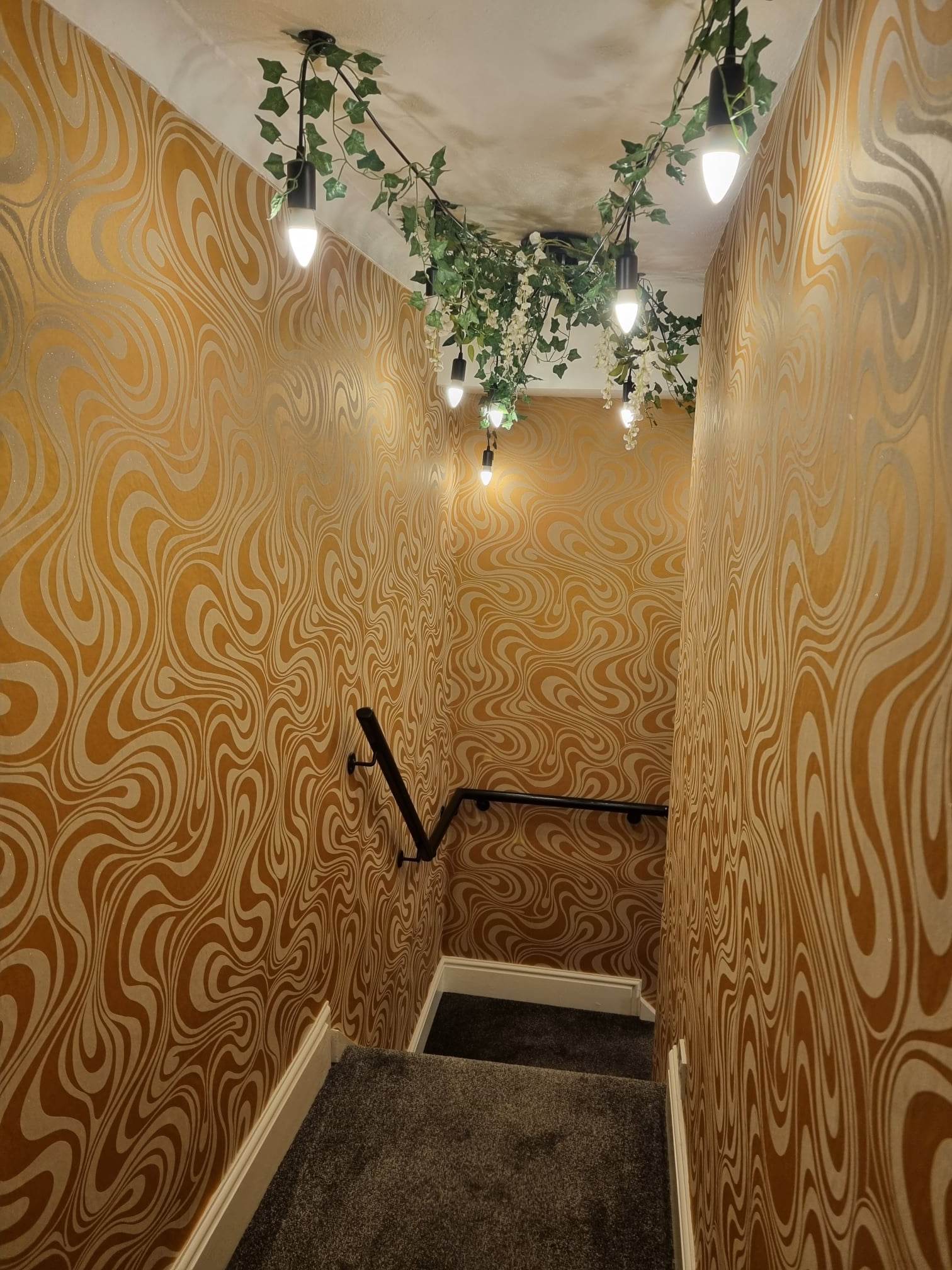 Staircase at Bella's Eden with gold swirl wallpaper and hanging vine lights
